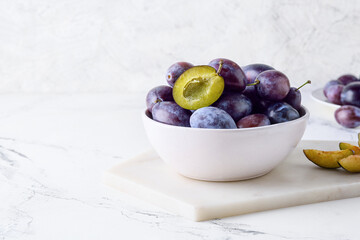Bowl with tasty plums on light background