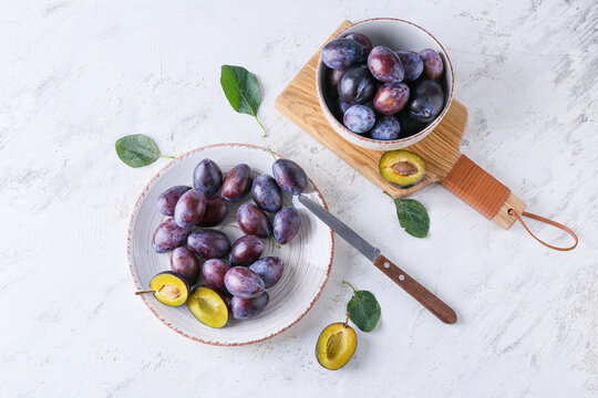 Plate with tasty plums on light background
