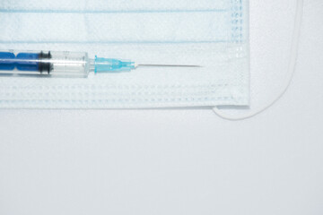 One single syringe with dose of medicine or vaccine with one single protective face mask on white...