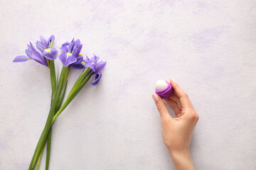 Obraz na płótnie Canvas Hand with lip balm and flowers on light background