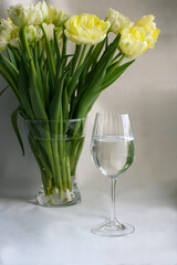 A glass of water on the background of a beautiful bouquet of tulips.