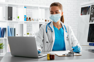 Young woman doctor sitting at working table using laptop