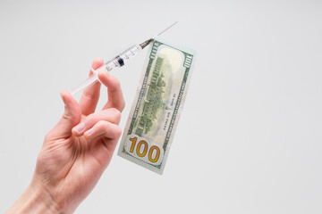Hand holds a medical syringe. A dollar bill is impaled on the syringe.