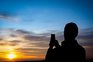 Silhouette of young man shoots sunset on phone, smartphone. Travel, walking.