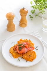 sweet potato pancakes with red fish and herbs on a white plate, selective focus