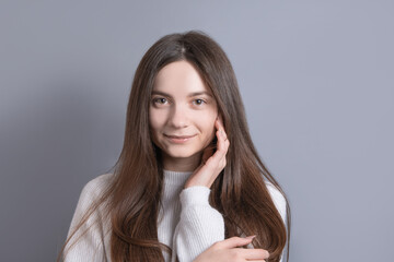 Portrait of a young attractive girl woman with dark long hair easily smiling on a gray studio background. Place for text. With copy space