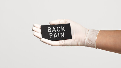 Closeup of the hand in a white sterile glove holding a card with text - BACK PAIN