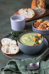 Broccoli cream soup decorated with thyme, cream, roasted cauliflower and fresh bread on green concrete background. Healthy vegetarian food concept.
