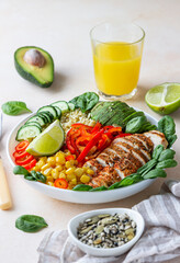 Healthy buddha bowl lunch with grilled chicken and bulgur, spinach, avocado, cucumber, bell pepper and corn on light background. Delicious balanced food concept.