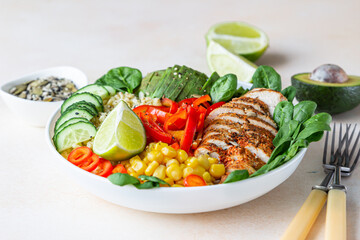 Healthy buddha bowl lunch with grilled chicken and bulgur, spinach, avocado, cucumber, bell pepper and corn on light background. Delicious balanced food concept.