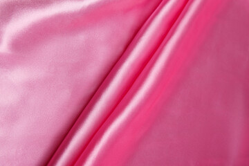 Colored pink textile satin fabric folded in folds and waves with highlights and texture