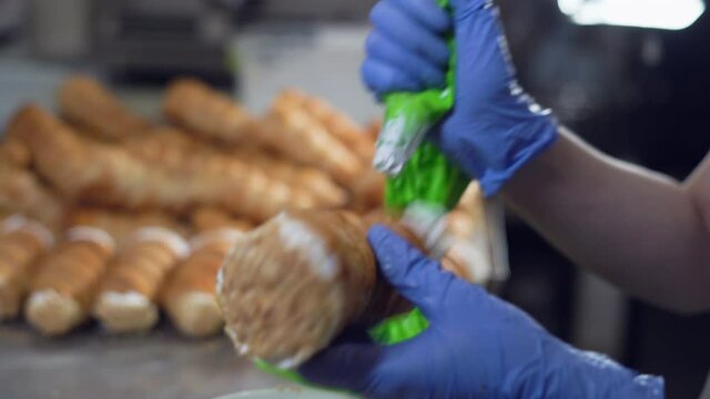 A woman fills the horns with cream from a pastry bag. Hands in gloves close up