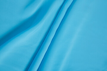 Colored blue textile satin fabric folded in folds and waves with highlights and texture