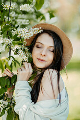 Young beautifull woman near bird cherry flowers. Bloomy bird cherry tree and happy woman in a hat. Spring time card.