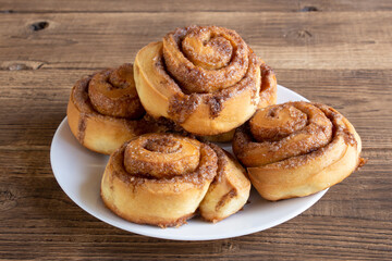 Cinnabon buns with sugar and cinnamon on a white plate on wooden background