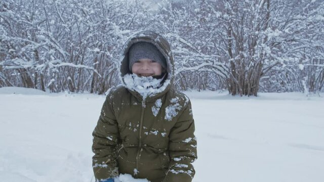 Portrait of smiling child playing with snow outdoors. Close up of boy having fun in winter park with friends in vacation and holidays. Emotion, happiness, lifestyle concept.
