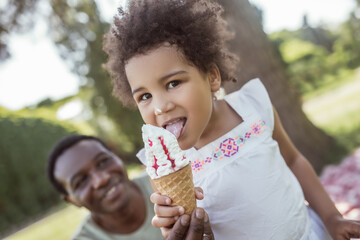 Dark-skinned cute kid eating ice-cream and spending time with dad