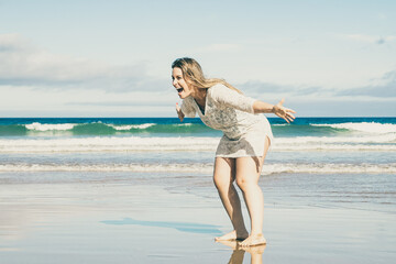 Cheerful excited woman bending and opening arms for catching and hugging child. Wet golden sand, blue sky and sea waves with white foam in background. Parenting and outdoor activities concept