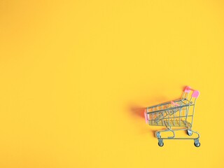 Shopping trolley on yellow background. Shopping cart in the supermarket. Sale, discount, shopaholism concept. The trend of consumer society. Top view with copy space.