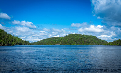 Blue lake in Quebec Province, Canada, with green forest on a hill in the background on a sunny day and blue sky 