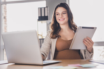 Photo portrait of pregnant mother holding tablet typing on laptop at desk in modern office