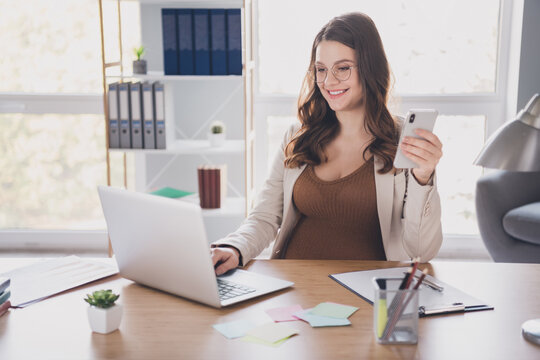 Photo of pregnant boss work laptop hold telephone wear glasses suit brown shirt workstation office indoors