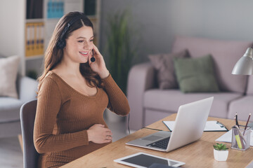 Photo of pregnant customer support adviser sit table hand belly wear headset brown shirt workstation office indoors