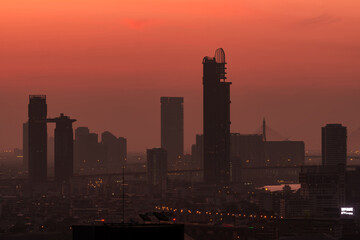 Cityscape in the morning with red sunrise sky. City covered with smog. Air pollution problem. Skyscraper building downtown. Urban skyline. Silhouette modern office and hotel building in town at dawn.