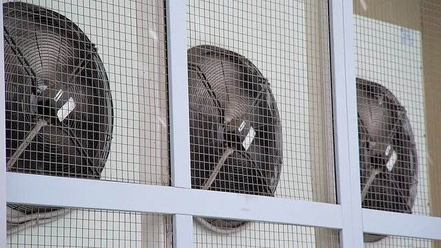 air conditioning fan propellers spin on the factory building behind bars in snowy weather