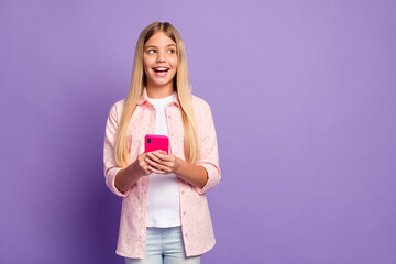 Photo of optimistic long hairdo pretty girl hold telephone look empty space wear pink shirt isolated on violet color background