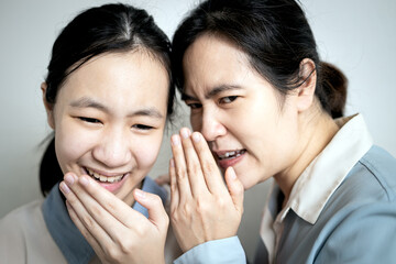Asian mother whispering gossiping in her daughter ear,adult woman look at other with...