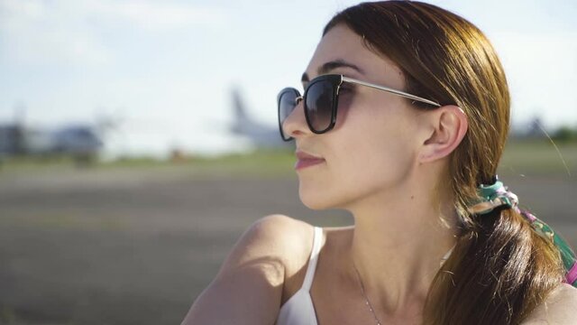 The girl with glasses turns from the camera. Background airplane