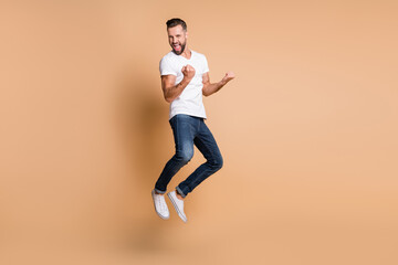 Fototapeta na wymiar Full length body size view of attractive cheerful guy jumping rejoicing victory isolated over beige pastel color background