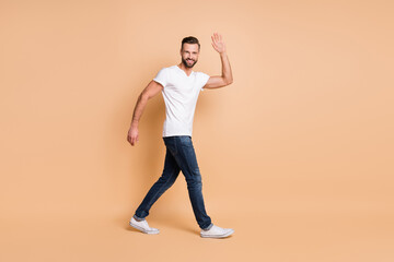 Fototapeta na wymiar Full body profile side photo of young man happy positive smile wave hi hello go walk isolated over beige color background