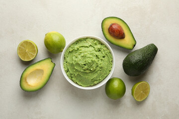 Bowl of guacamole, avocado and lime on white textured background, top view