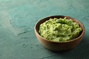Bowl of guacamole on green textured background, space for text