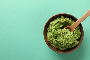 Bowl of guacamole with spoon on mint background, space for text