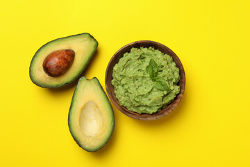 Bowl of guacamole and avocado on yellow background, top view