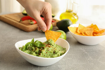 Female hand dips chips slice in guacamole