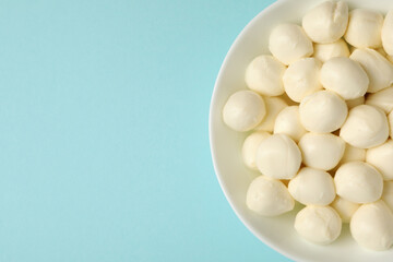 Bowl with fresh mozzarella cheese on blue background