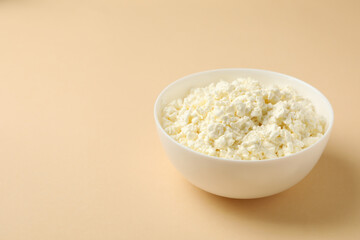 Bowl with fresh cottage cheese on beige background