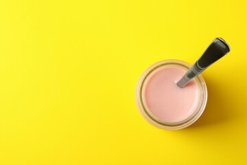 Glass jar with spoon and yogurt on yellow background