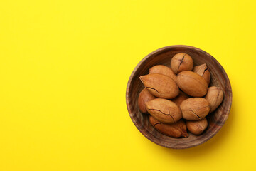 Bowl with tasty pecan nuts on yellow background