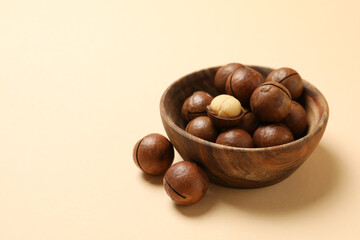Bowl with tasty macadamia nuts on beige background