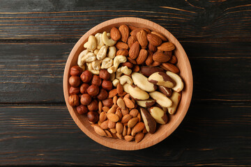 Bowl with different nuts on wooden background, top view