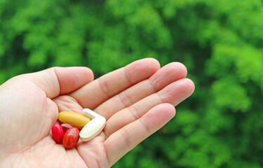 Assorted Supplement Tablets in Hand with Blurry Green Foliage in the Backdrop