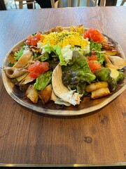 grilled chicken salad with chopped eggs, lettuce, mushrooms, tomatoes, potatoes and cheese on a brown wooden table.