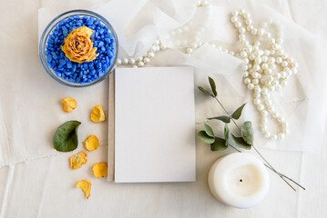 Fototapeta na wymiar Layout scene of a stationery layout. An empty vertical greeting card, a string of pearls and dried flowers isolated on a white table background. Top view blank for invitation