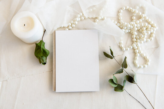 Layout scene of a stationery layout. An empty vertical greeting card, a string of pearls and dried flowers isolated on a white table background. Top view blank for invitation