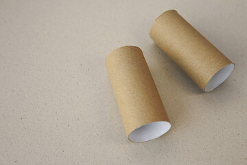 Two toilet paper roles lying down horizontally made of recycled brown paper or cardboard on a similar beige coloured background with negative space